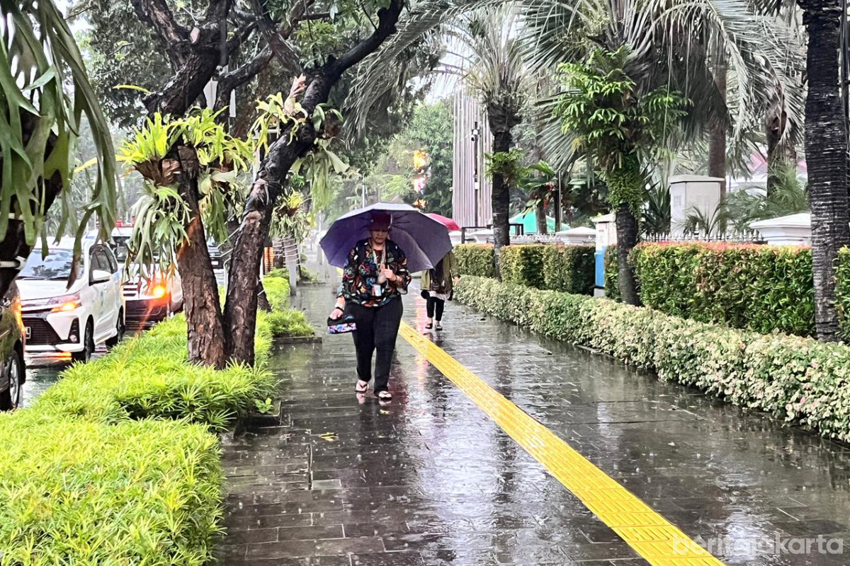 Seorang warga menggunakan payung berjalan di trotoar