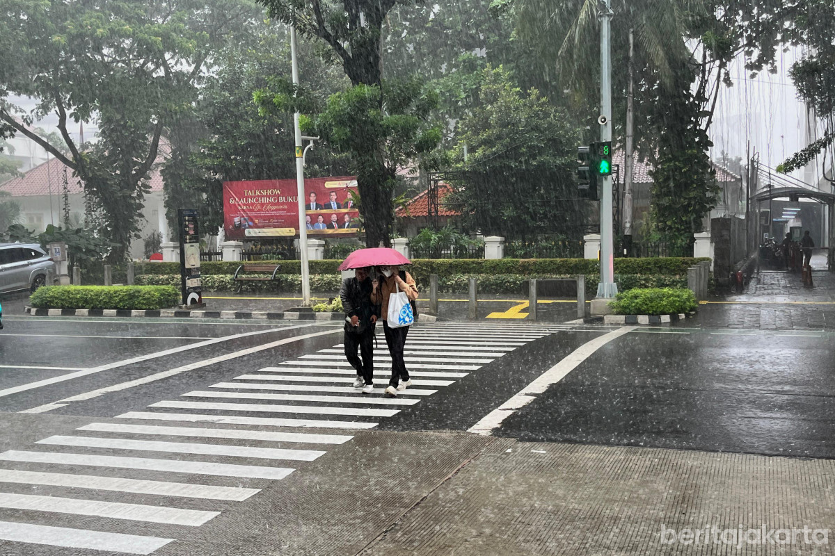 Warga menggunakan payung menyeberangi jalan saat cuaca hujan