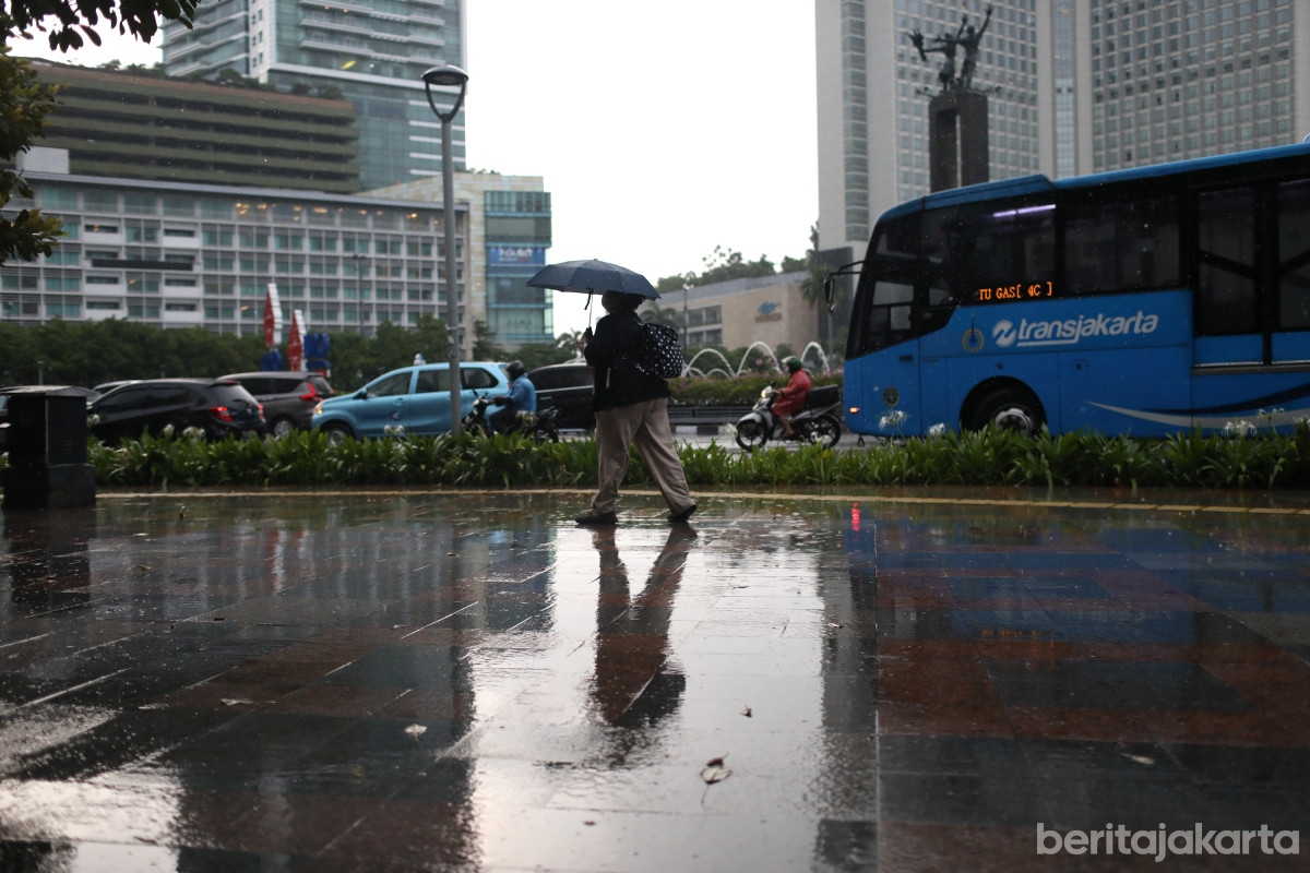 Seorang warga menggunakan payung berjalan di kawasan Bundaran HI