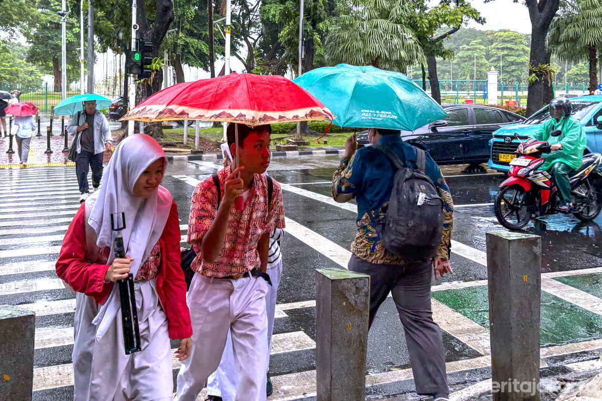 Warga menggunakan payung menyebrang jalan saat hujan
