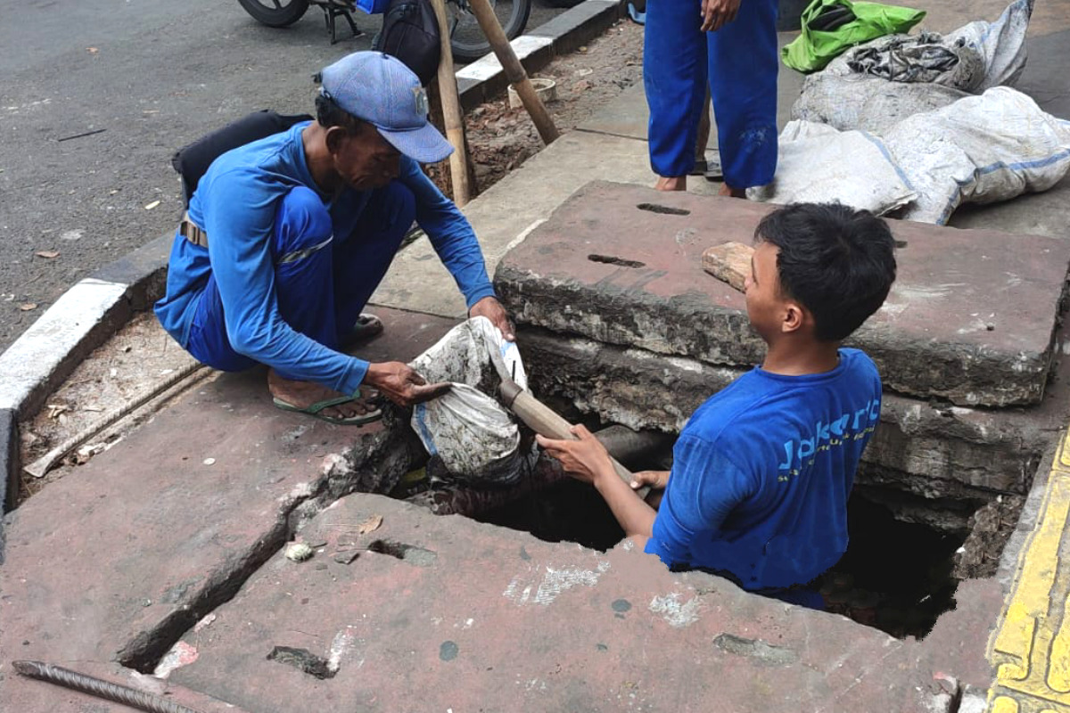 Pasukan Biru Kuras Saluran Air di Jalan Stasiun Pasar Senen 