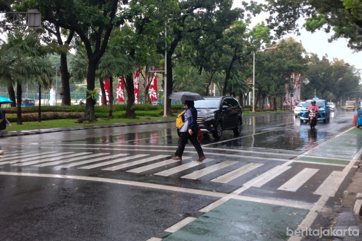 Seorang warga menyeberangi jalan dengan payung saat hujan