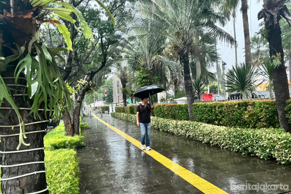 Seorang warga menggunakan payung berjalan di trotoar saat cuaca hujan