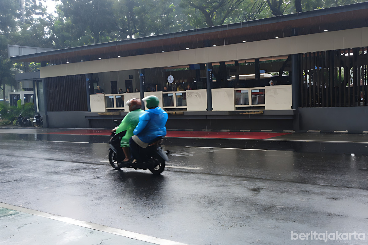 Pengendara motor melintas di depan halte transjakarta saat hujan